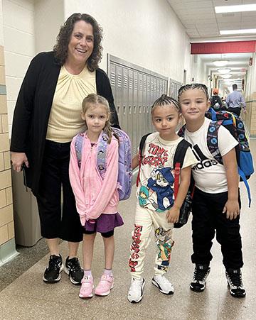 Three students in a school hallway next to their teacher.